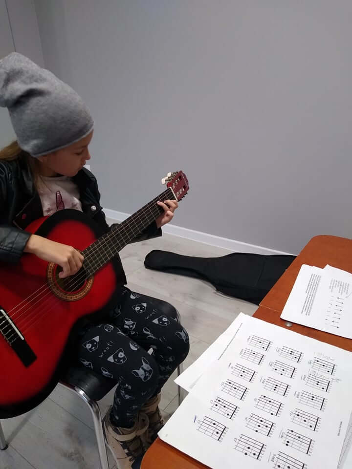 Zdjęcie przedstawia dziewczynkę grającą na gitarze