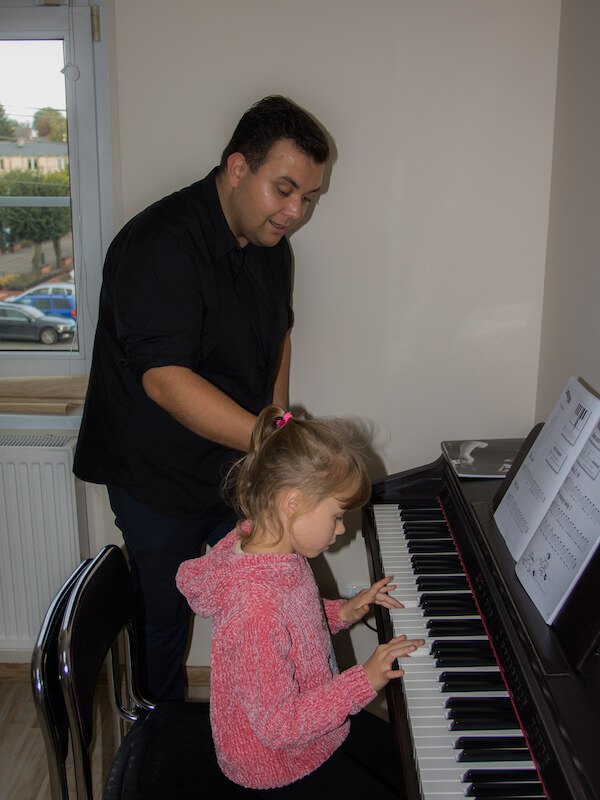 Zdjęcie przedstawia dziecko grające na pianinie pod okiem instruktora